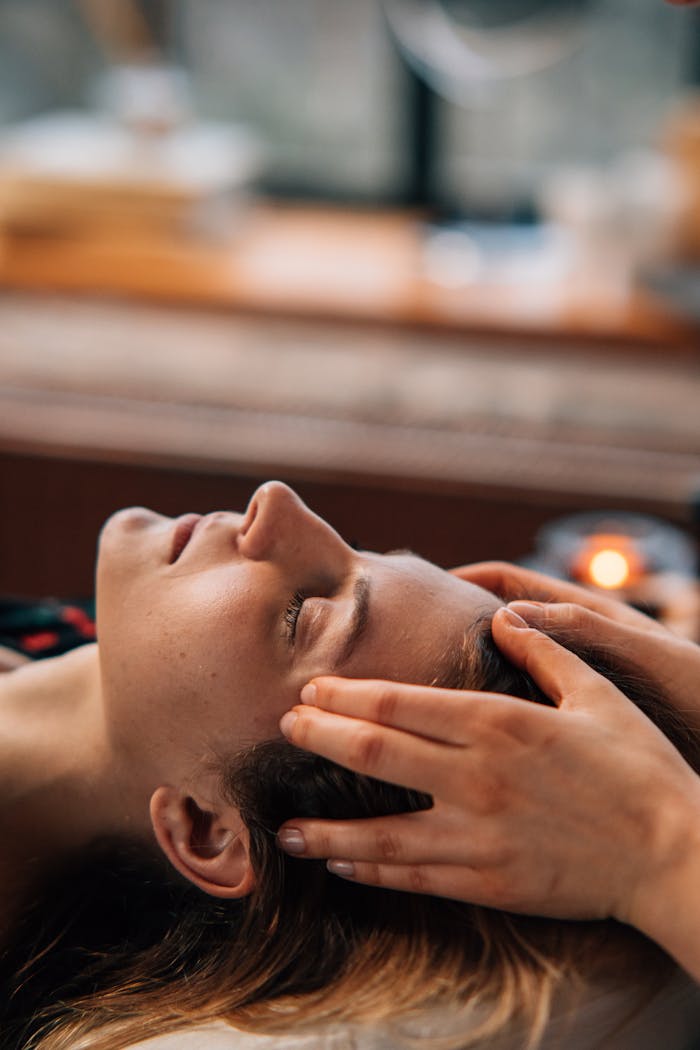 Woman enjoying a relaxing face massage indoors, eyes closed, with hands gently massaging temples.